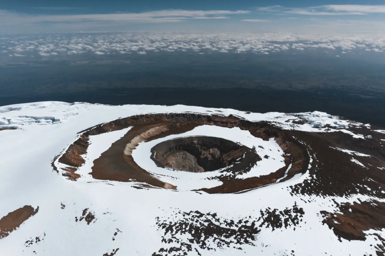Aerial view of Mount Kilimanjaro's snow-rimmed Reusch Crater near the summit, rising above a sea of clouds